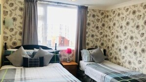 Une chambre avec deux lits, un papier peint à motifs floraux et une fenêtre avec des rideaux.
