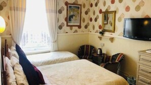 Una habitación de hotel con dos camas, televisión, cómoda y ventana con cortinas.