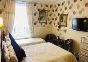 Una habitación de hotel con dos camas, televisión, cómoda y ventana con cortinas.