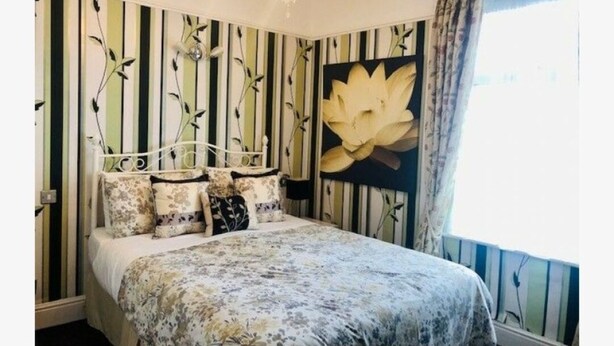Une chambre à coucher avec un lit, un lustre, un papier peint à rayures et un grand tableau représentant des fleurs.
