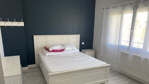 A bedroom with a bed, bedside tables, a window with curtains, and a wall-mounted coat rack. - Villa Royan 10 persons with private heated pool 650m from the beach (Royan)