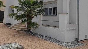 A two-story building with a balcony, a palm tree, and a paved driveway. - Villa Royan 10 persons with private heated pool 650m from the beach (Royan)