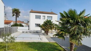 A two-story house with a swimming pool, a fenced yard, and palm trees. - Villa Royan 10 persons with private heated pool 650m from the beach (Royan)