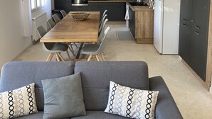 A modern kitchen with a dining area, featuring a wooden table, grey sofa, and pendant lighting. - Villa Royan 10 persons with private heated pool 650m from the beach (Royan)