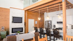 Interior moderno de una cabaña de troncos con comedor, cocina y una zona de estar acogedora con chimenea.