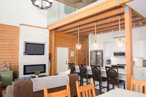 L’intérieur d’une maison en rondins moderne comprend un coin repas, une cuisine et un espace salon confortable avec une cheminée.