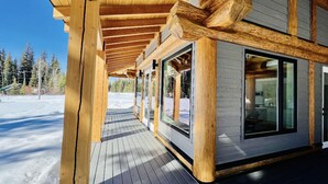 Una terraza de madera con zona cubierta, ventanas amplias y vistas a un paisaje nevado.