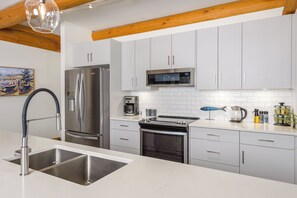 Una cocina moderna con electrodomésticos de acero inoxidable, armarios blancos y techo de madera.
