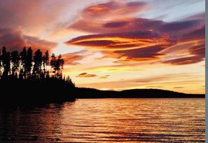 A sunset over a body of water with a silhouette of a forested landmass.