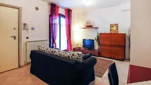 A living room with a sofa, a television, a wooden cabinet, and a window with curtains. - Lovely home in Porto Recanati with WiFi (Porto Recanati)