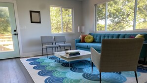 A modern living room with a blue sofa, grey chairs, a coffee table with books, and a patterned rug.