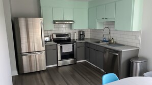 A modern kitchen with stainless steel appliances, teal cabinets, and a white tiled backsplash.