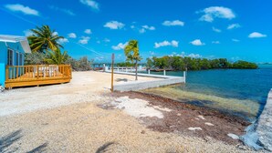A beachside property with a wooden deck, a concrete pier, and a clear view of the turquoise sea. - Haven House (Little Torch Key)