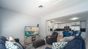 A modern living room with a flat-screen TV, comfortable seating, and a kitchen in the background. - Haven House (Little Torch Key)