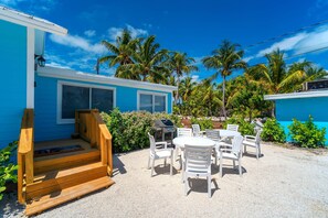 A blue building with a wooden deck, a barbecue grill, and white outdoor furniture.