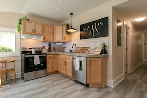 A modern kitchen with wooden cabinets, stainless steel appliances, and a black artwork on the wall. - TWO king bedrooms! Walk to EVERYTHING! (lake,hiking,bars,shopping) (Watkins Glen)
