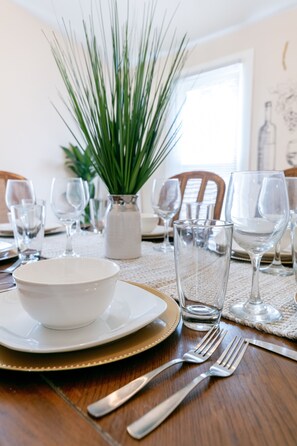 A dining table set with white plates, gold-rimmed bowls, and clear wine glasses. - TWO king bedrooms! Walk to EVERYTHING! (lake,hiking,bars,shopping) (Watkins Glen)