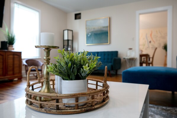 A living room with a round wooden table, a white vase with green plants, a brass candle holder, and a blue sofa. - TWO king bedrooms! Walk to EVERYTHING! (lake,hiking,bars,shopping) (Watkins Glen)