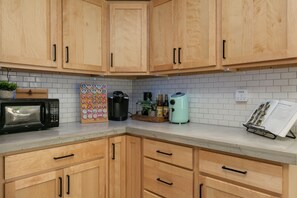 A kitchen with wooden cabinets, a microwave, a coffee maker, and a cookbook on the counter. - TWO king bedrooms! Walk to EVERYTHING! (lake,hiking,bars,shopping) (Watkins Glen)