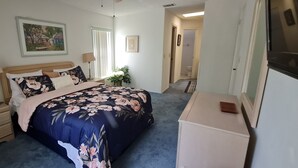 Ein Schlafzimmer mit Bett, Nachttischen, einem Schminktisch, einer Lampe, einem gerahmten Bild und einer Pflanze.
