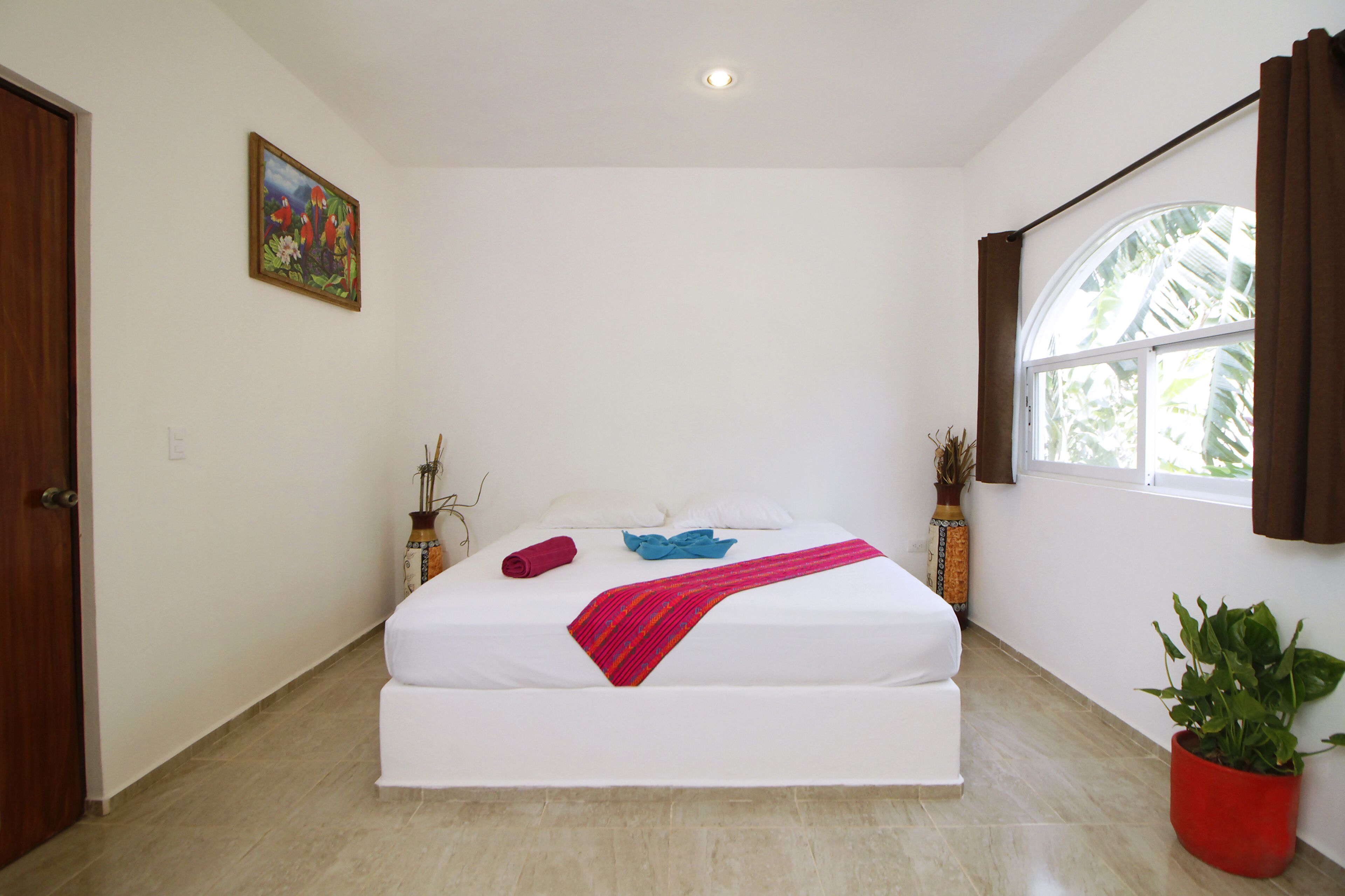Une chambre à coucher avec un grand lit, une fenêtre avec des rideaux, une plante en pot et un tableau accroché au mur.