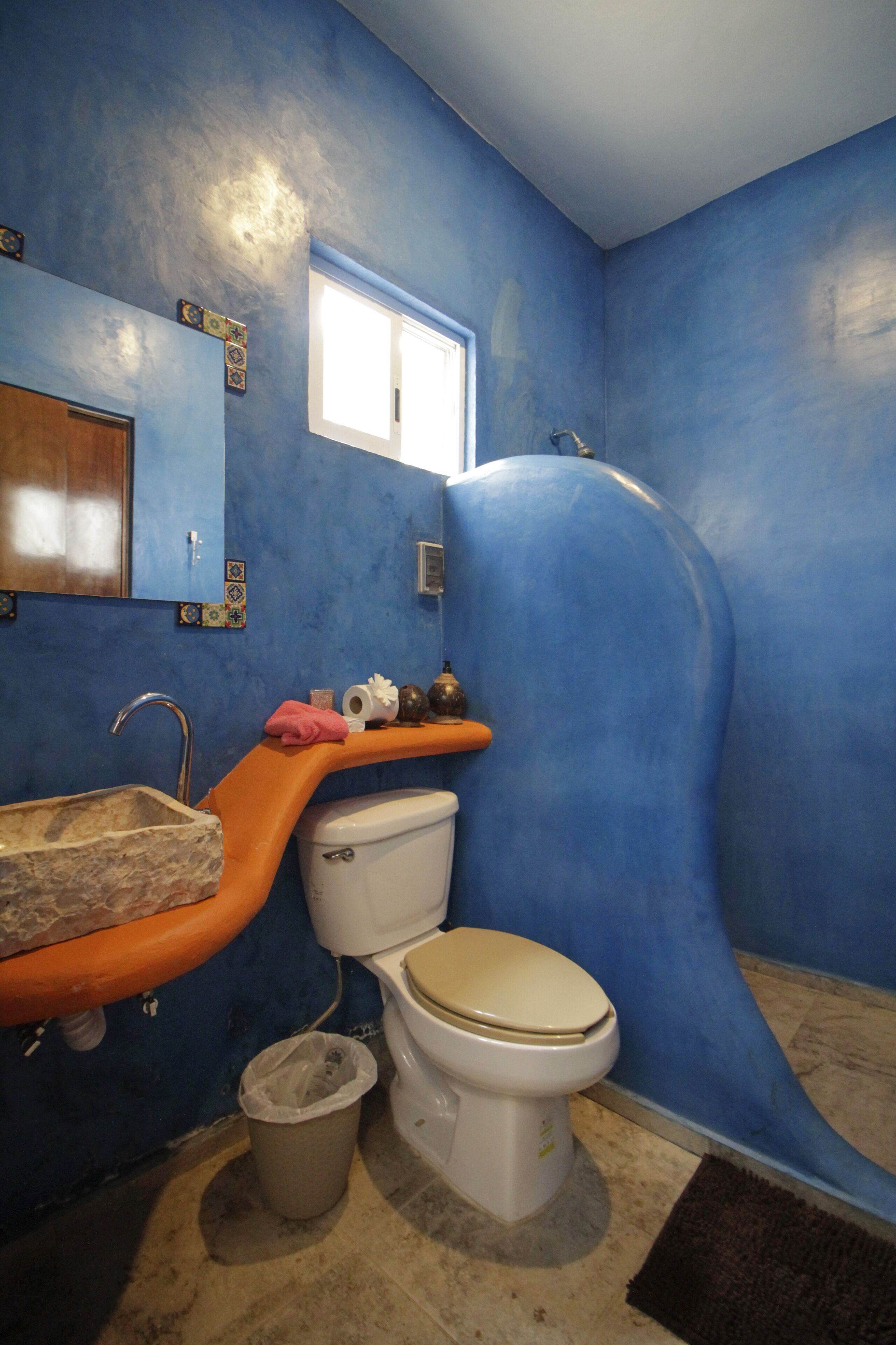Une salle de bain avec un mur bleu, des toilettes blanches, un lavabo avec un plan de toilette orange et un espace douche.