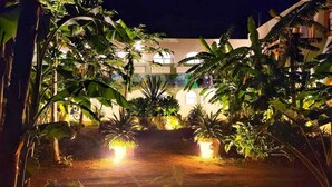 A nighttime view of a building surrounded by lush vegetation and illuminated by warm lights. - Coco Resort (Motul)