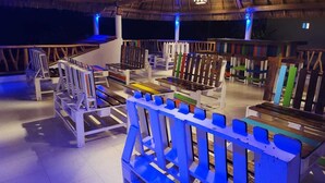 A spacious room with a high ceiling and a thatched roof, featuring a variety of seating arrangements and a central staircase.