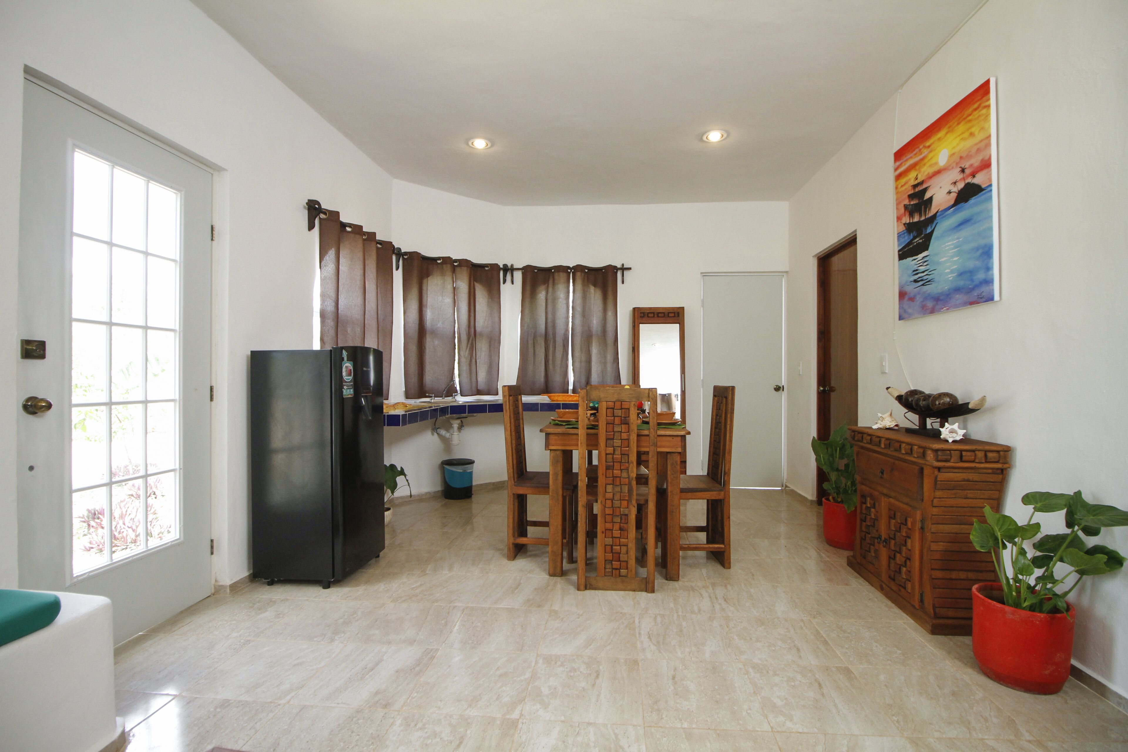 A dining area with a table and chairs, a refrigerator, and potted plants.