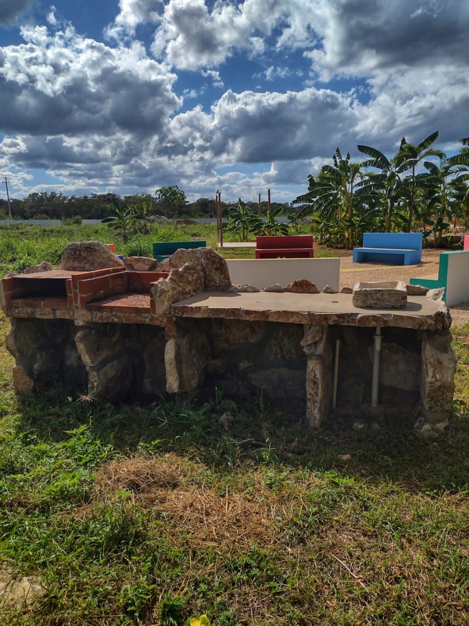 An outdoor stone structure with benches and a grassy area.