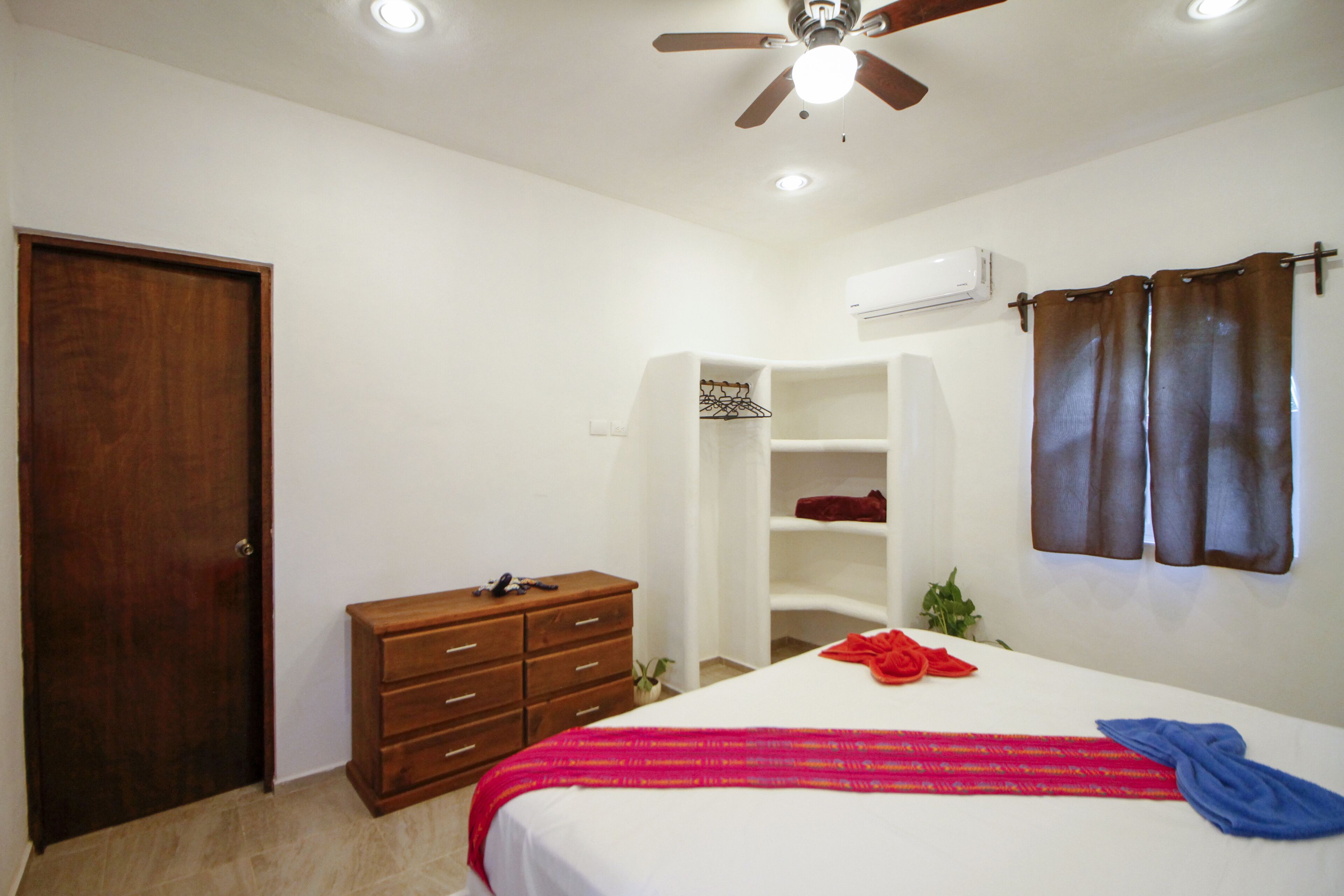 Une chambre à coucher comprenant un lit, une commode en bois, une armoire, un ventilateur de plafond et un appareil de climatisation.