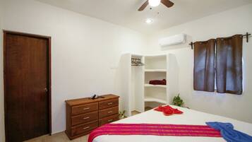 Une chambre à coucher comprenant un lit, une commode en bois, une armoire, un ventilateur de plafond et un appareil de climatisation.