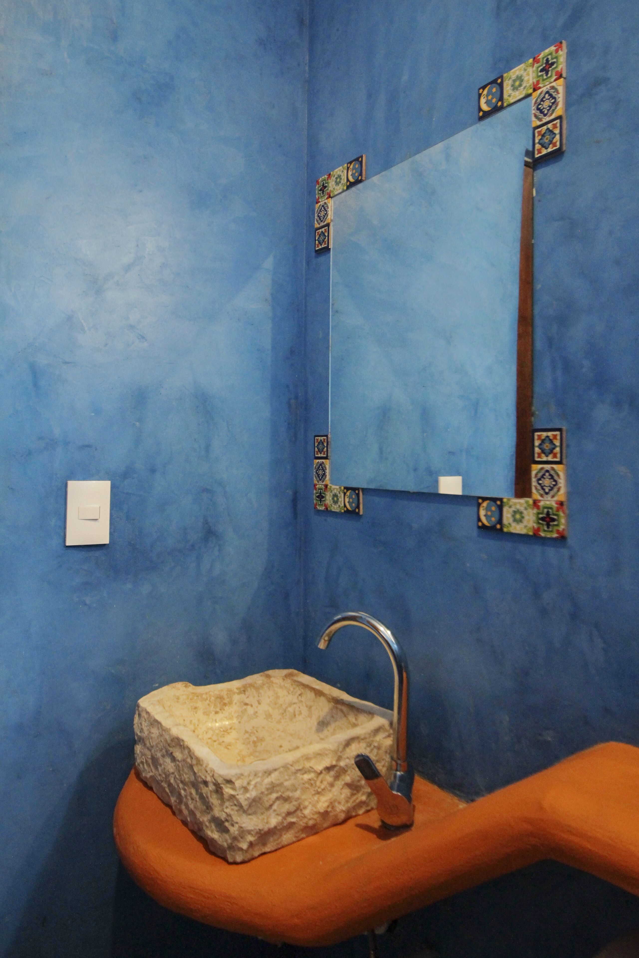 Une salle de bain avec un mur bleu, un lavabo blanc doté d’une cuve en pierre et un miroir orné de motifs décoratifs.