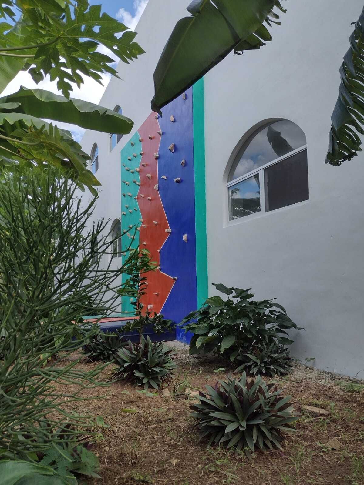 Un edificio con un diseño vertical colorido, una ventana y vegetación circundante.