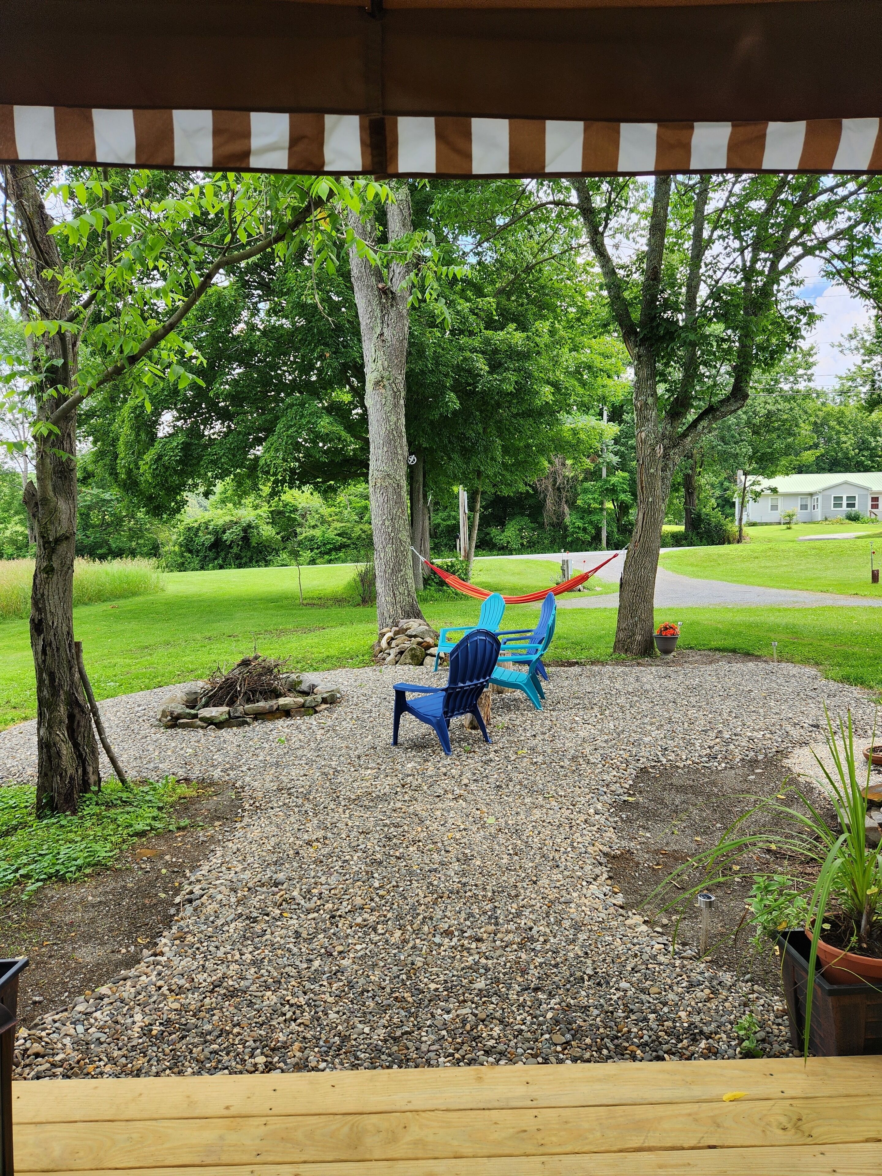 A patio area with a hammock, two Adirondack chairs, and a wooden deck.