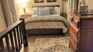 A bedroom with a bed, a nightstand, a dresser, a clock, and a wall-mounted shelf.