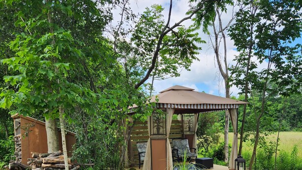 A gazebo with a wooden deck, surrounded by a garden with rocks and plants.