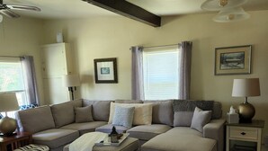 A living room with a sectional sofa, a coffee table, a side table, a lamp, a picture frame, and a ceiling fan.