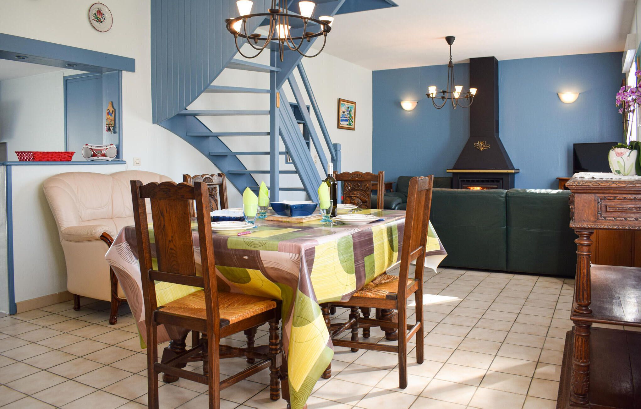 A dining area with a table set for four, surrounded by wooden chairs. A staircase is visible in the background, leading to an upper level.
