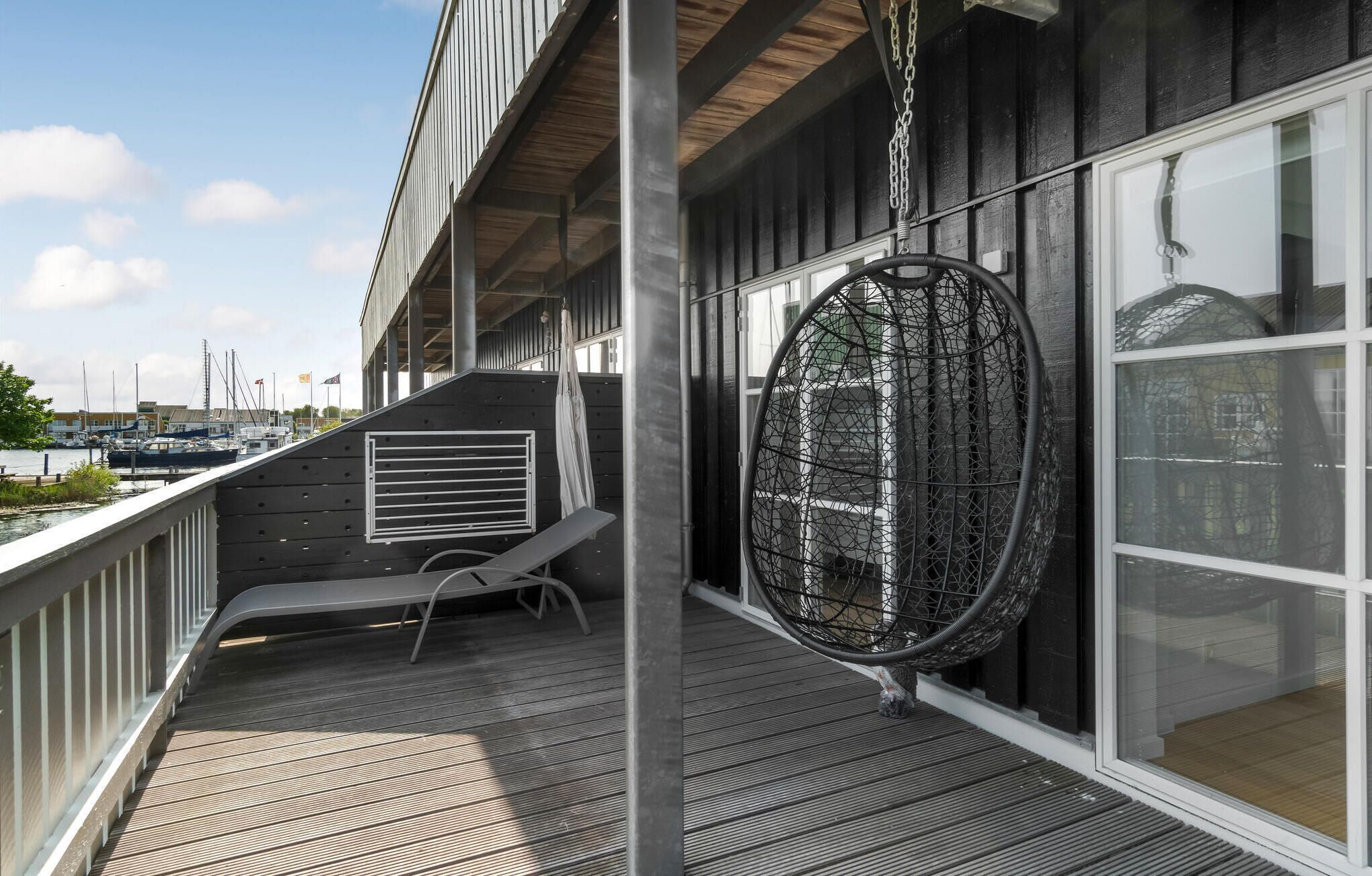 A balcony with a seating area, a hanging chair, and a view of boats in the background.