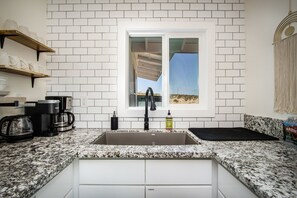 Una cucina con piastrelle bianche a metro, un piano di lavoro in granito, un lavello doppio, una macchina da caffè e una finestra con vista su un paesaggio desertico.