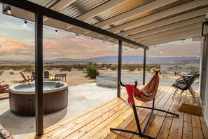 A wooden deck with a hot tub, chairs, and a hammock.
