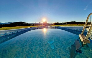 Ein klares Schwimmbecken mit Blick auf einen Sonnenuntergang über einer hügeligen Landschaft.
