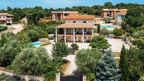Une villa à plusieurs étages avec une piscine, entourée d’une végétation luxuriante et d’oliviers.