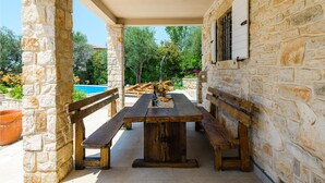 Un espace extérieur aménagé pour les repas, avec des murs en pierre, des bancs en bois et une piscine en arrière-plan.