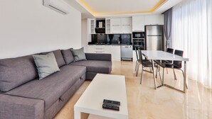 Una sala de estar moderna con un sofá gris, una mesa de centro blanca y un comedor con una mesa y sillas blancas.