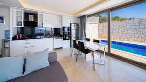 Una cocina moderna con armarios blancos, un comedor con mesa y sillas, y vistas a una piscina a través de amplios ventanales.