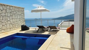 Una piscina en la azotea con pared de piedra, sillas de descanso y vistas al mar.