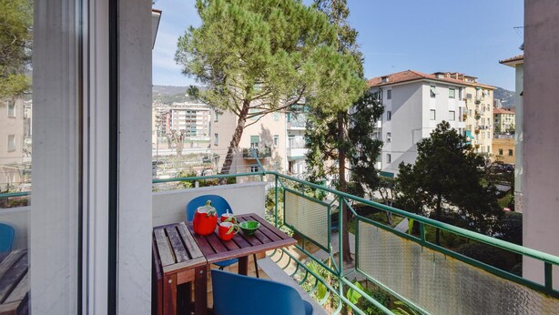 Un balcon avec une table, des chaises et une vue sur les bâtiments et les arbres.