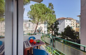 Een balkon met een tafel, stoelen en uitzicht op gebouwen en bomen.